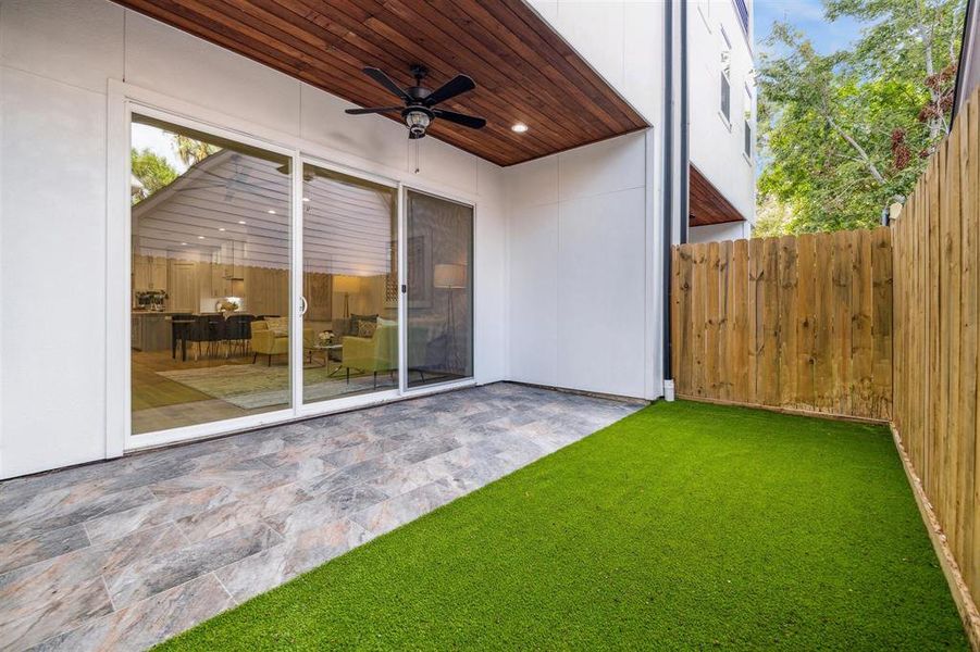 Backyard with covered patio, ceiling fan, and turf for easy maintenance.