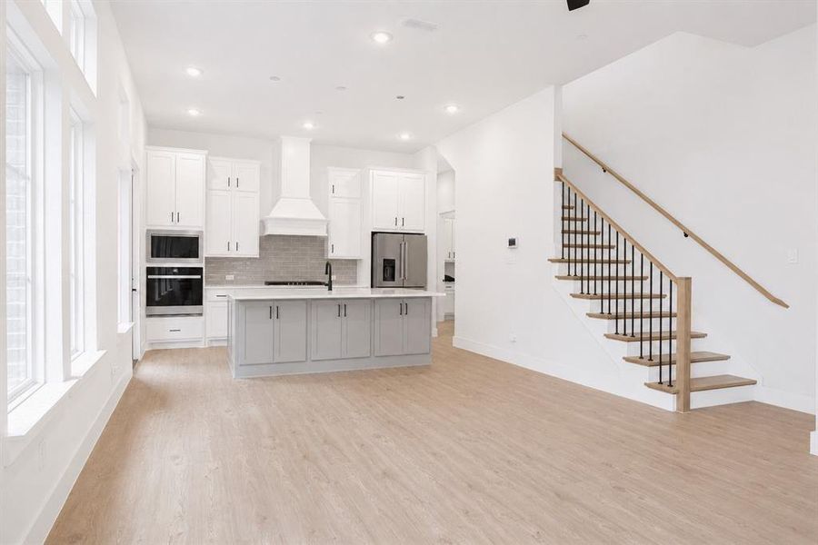 Open-concept kitchen with white cabinetry, a light gray island, stainless steel appliances, and wood-finish flooring