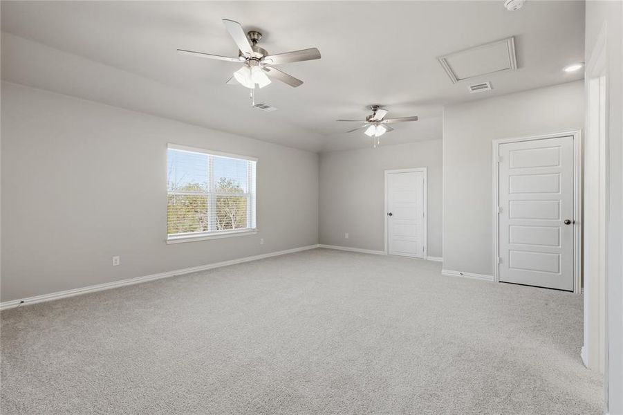 Spacious room featuring light gray carpeting, two ceiling fans with integrated lighting, a single window with blinds, and white panel doors
