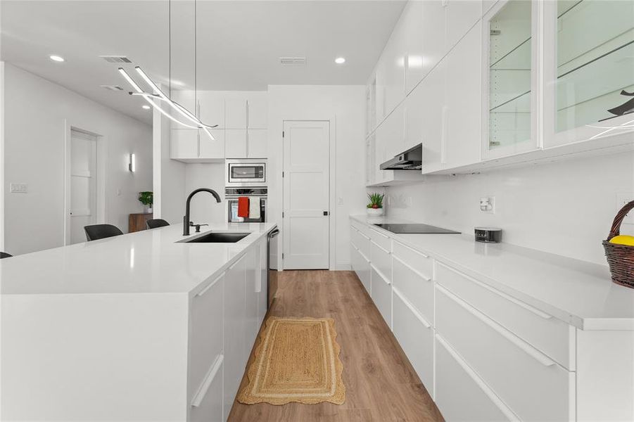 Kitchen with white cabinetry, light stone counters, light wood finished floors, hanging light fixtures, and stainless steel appliances