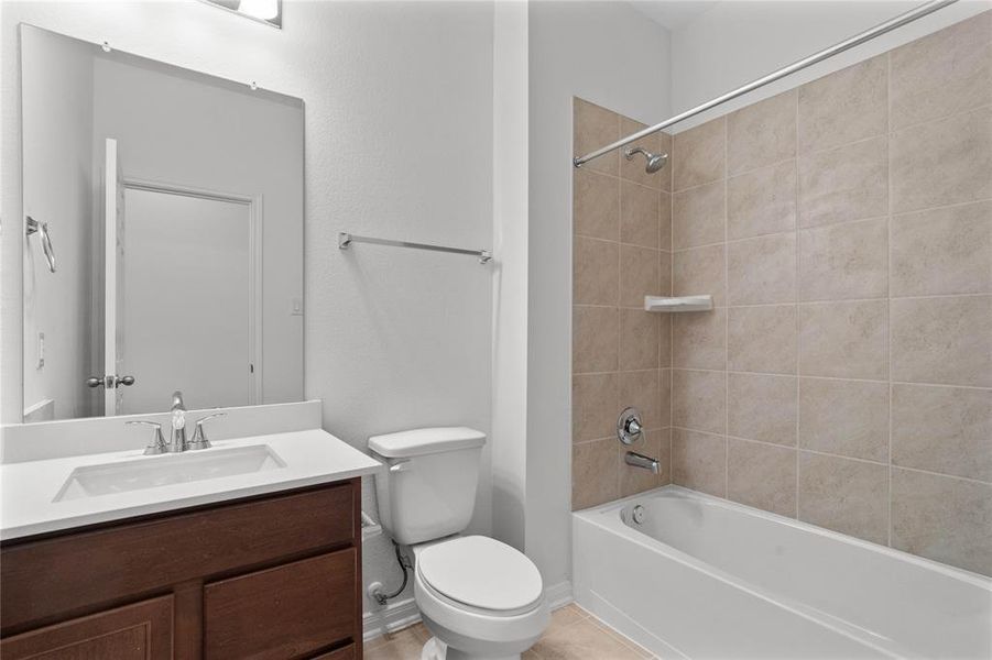 Secondary bathroom features light countertops and stained cabinets, neutral paint, shower/tub combo with tile surround, large mirror, tile floors, sleek fixtures and modern finishes, plenty of space to accommodate any visiting family or guests.