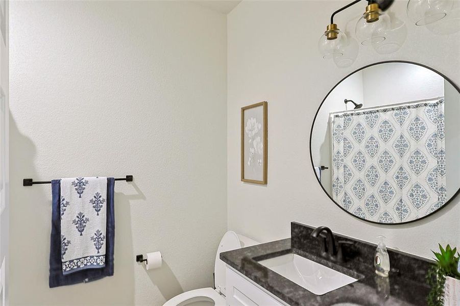 Bathroom featuring a dark countertop vanity with an integrated sink, a circular black-framed mirror, and a modern three-light fixture
