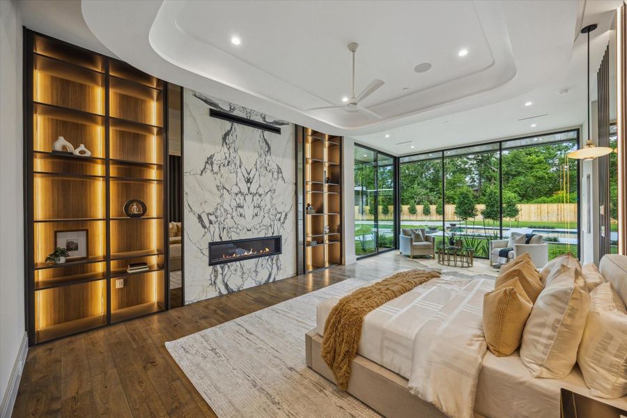 A true sanctuary, the primary suite exudes modern luxury with floor-to-ceiling glass walls, a dramatic bookmatched marble fireplace, and illuminated custom shelving. Soaring ceilings, rich hardwood flooring, and serene pool views complete this showstopping retreat.A true sanctuary, the primary suite exudes modern luxury with floor-to-ceiling glass walls, a dramatic bookmatched marble fireplace, and illuminated custom shelving. Soaring ceilings, rich hardwood flooring, and serene pool views com