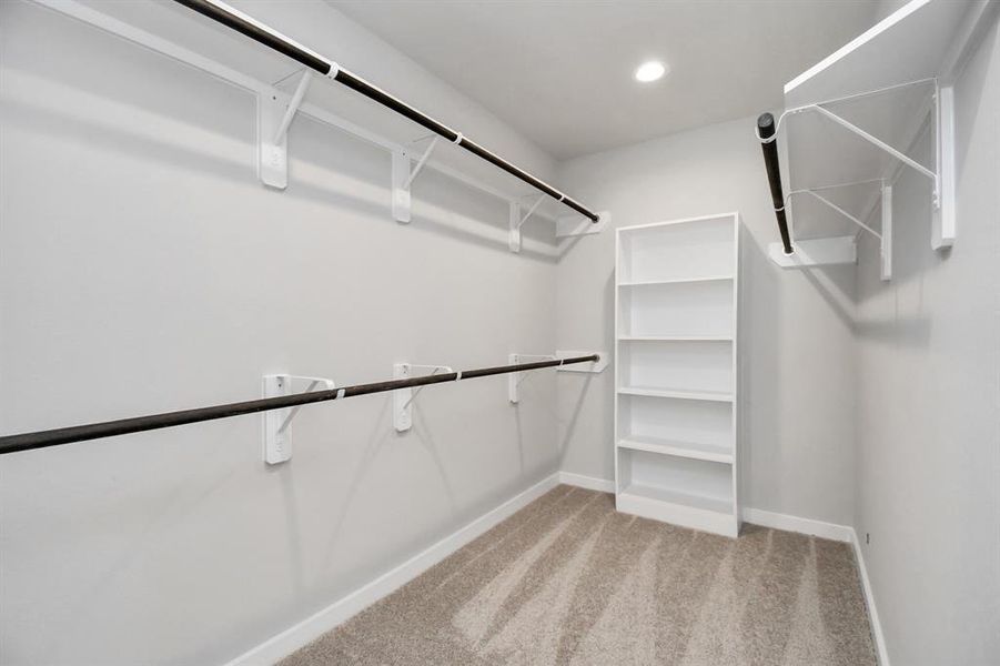 walk-in closet boasting high ceilings and plush carpeting. Let the inviting ambiance of warm paint tones surround you, make use of the practicality of built-in shelving, and revel in the contemporary and functional escape enriched by dark finishes. Sample photo of completed home. As-built color and selections may vary.