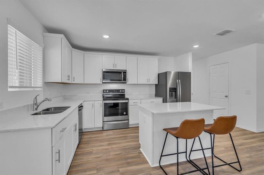Kitchen featuring stainless steel appliances, a breakfast bar, white cabinets, a center island, and light stone countertops