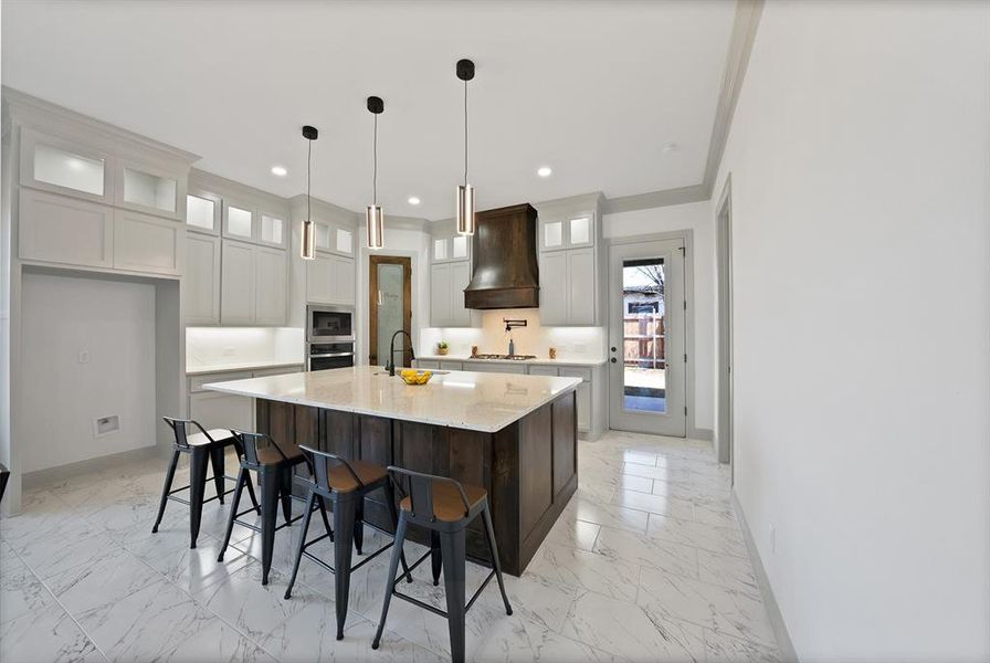Kitchen featuring glass insert cabinets, a spacious island, a breakfast bar area, light marble finish floors, and ornamental molding