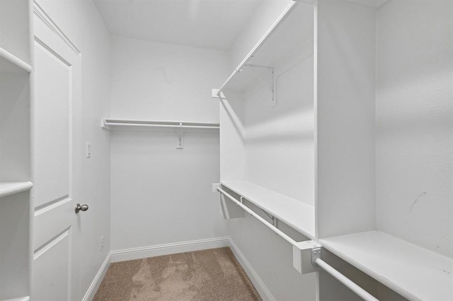 Walk-in closet featuring built-in shelving, multiple hanging rods, and neutral carpet flooring Walk-in closet featuring built-in shelving, multiple hanging rods, and neutral carpet flooring