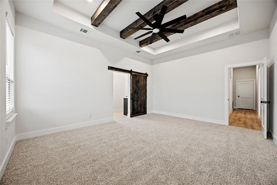 Carpeted empty room with a barn door, a ceiling fan, and a tray ceiling