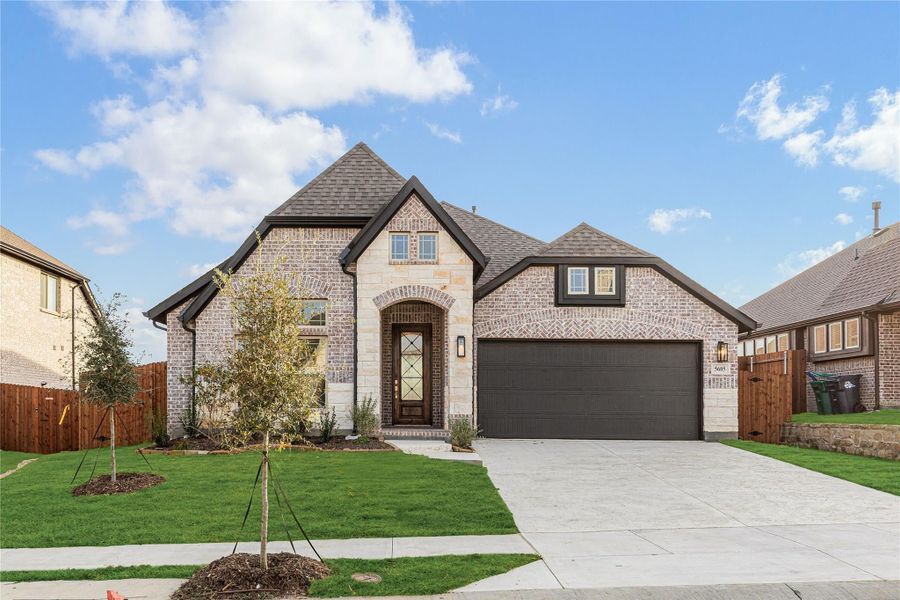 Single-story brick home with arched entry, two-car garage, and manicured front lawn