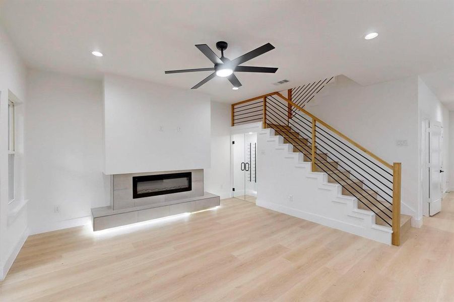 Unfurnished living room with wood finished floors, a tiled fireplace, stairway, recessed lighting, and a ceiling fan Unfurnished living room with wood finished floors, a tiled fireplace, stairway, recessed lighting, and a ceiling fan