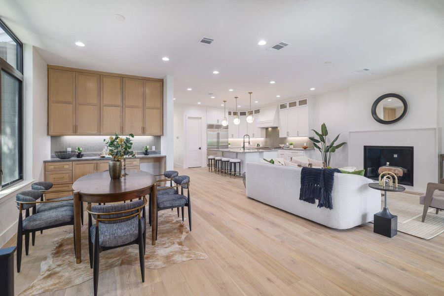 Open-concept living area featuring light wood-finish flooring, recessed lighting, a built-in fireplace, and a kitchen with an island and pendant lighting