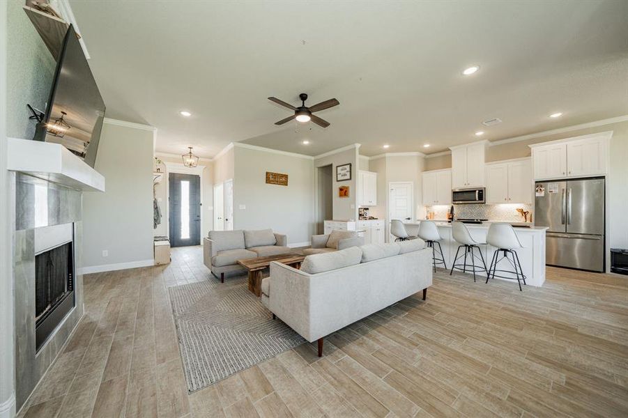 Living room with ornamental molding, a fireplace, recessed lighting, ceiling fan, and light wood-style floors Living room with ornamental molding, a fireplace, recessed lighting, ceiling fan, and light wood-style floors