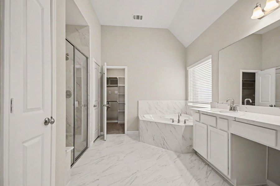 Luxurious bathroom featuring a spacious walk-in shower, elegant soaking tub, dual vanity all accented with stylish marble finishes.