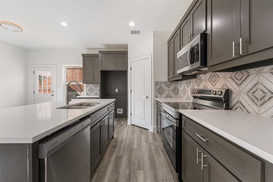 Kitchen featuring appliances with stainless steel finishes, backsplash, recessed lighting, a kitchen island with sink, and light wood-style flooring