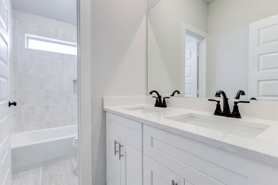 This shared upstairs bathroom delivers modern convenience with dual sinks, quartz countertops, and black faucets. Perfectly positioned to serve two secondary bedrooms, it’s designed for both efficiency and style.