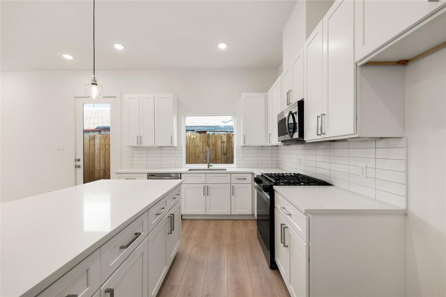 The kitchen comes equipped with stainless steel appliances, quartz countertops, beautiful white cabinetry and modern backsplash, high ceilings with recessed lighting, kitchen island with pendant lighting, and large window over the sink for natural lighting.