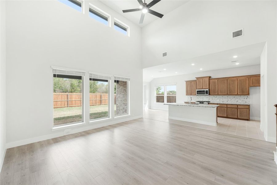 Open living area with high ceilings, ceiling fan, light wood floors, and open kitchen with wood cabinets in background