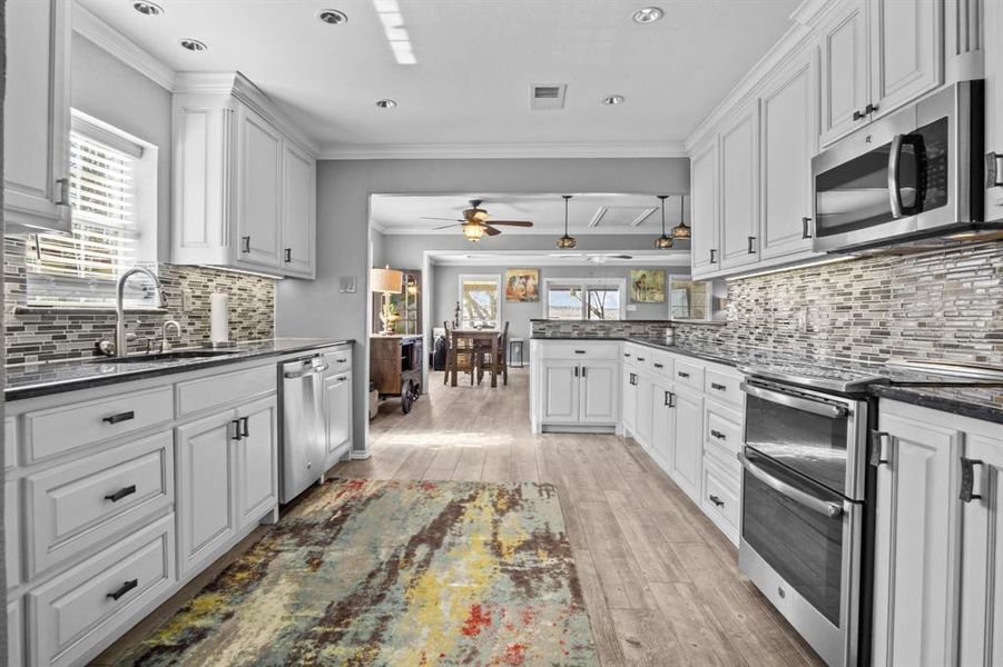 Kitchen featuring white cabinetry, dark stone counters, light hardwood / wood-style floors, crown molding, and stainless steel appliances