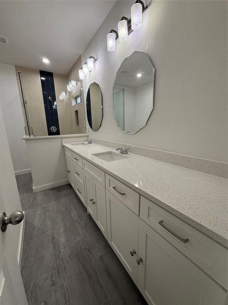 Bathroom featuring tiled shower, a sink, visible vents, and double vanity