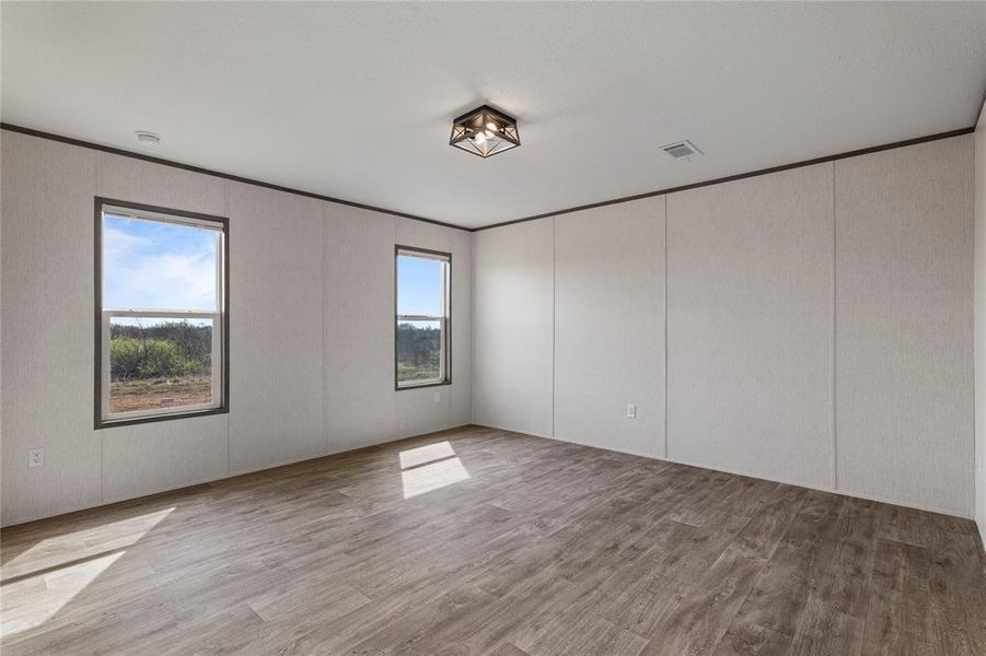 Unfurnished room featuring light wood-style flooring, crown molding, and a decorative wall