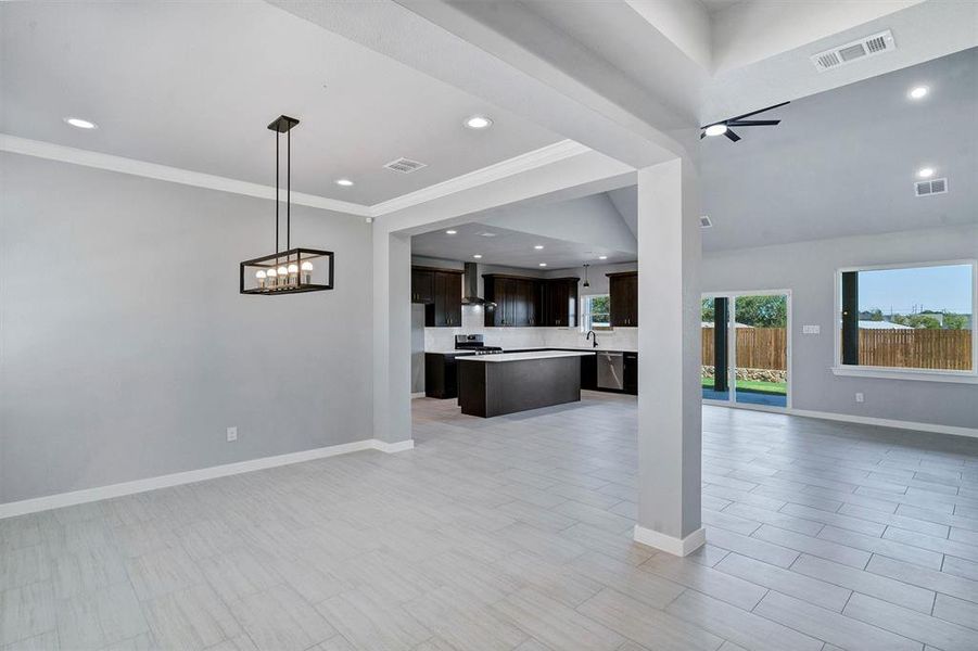 Unfurnished living room featuring ceiling fan with notable chandelier and ornamental molding