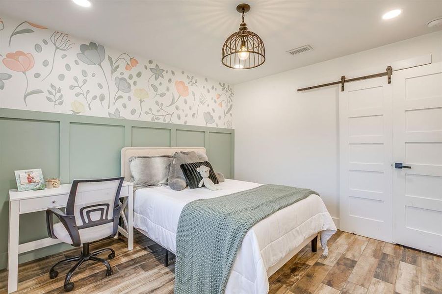 Bedroom with a decorative wall, wallpapered walls, a barn door, light wood-style floors, and recessed lighting
