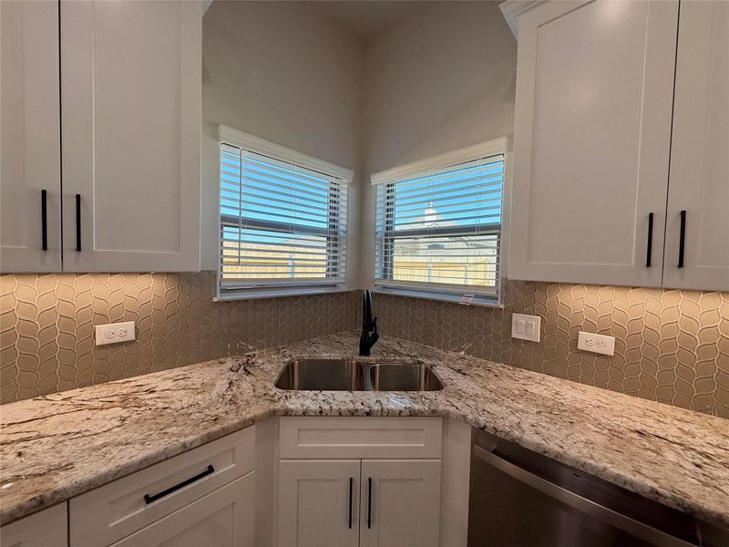 Kitchen with white cabinets, light stone counters, stainless steel dishwasher, and decorative backsplash