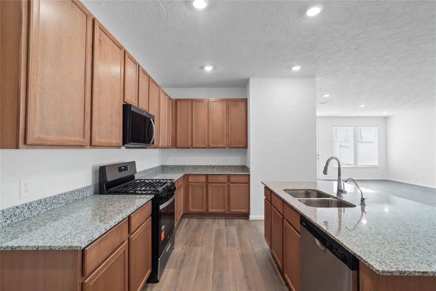 This bright, open kitchen is a chef's delight, complete with a large island, granite countertops, stained Woodmont Cody cabinets, Whirlpool stainless steel appliances, and modern Daltile backsplash.