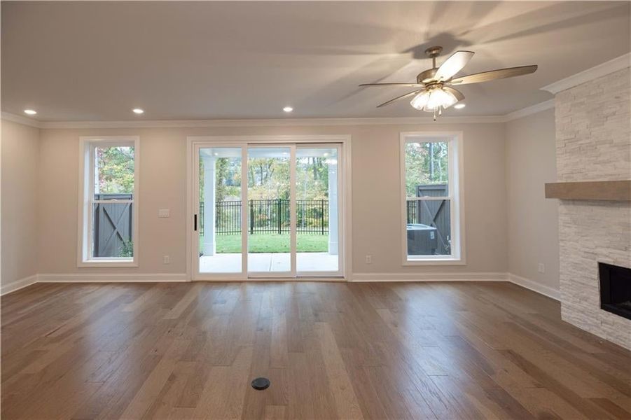 Unfurnished living room featuring crown molding, dark wood-style flooring, a stone fireplace, a ceiling fan, and recessed lighting