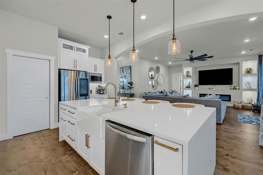 Kitchen with white cabinets, stainless steel appliances, sink, hanging light fixtures, and a center island with sink