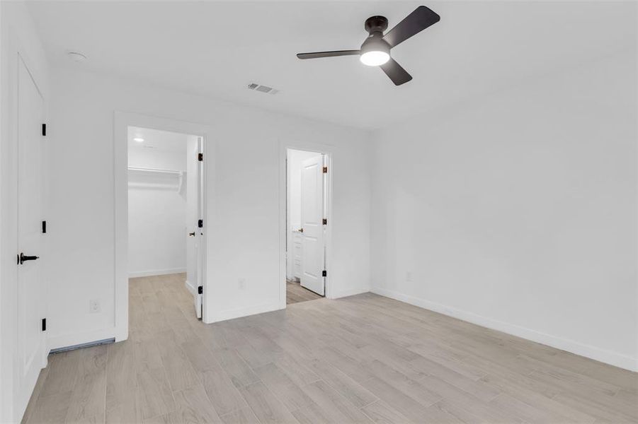 Unfurnished bedroom with a walk in closet, light wood-type flooring, ceiling fan, and ensuite bath