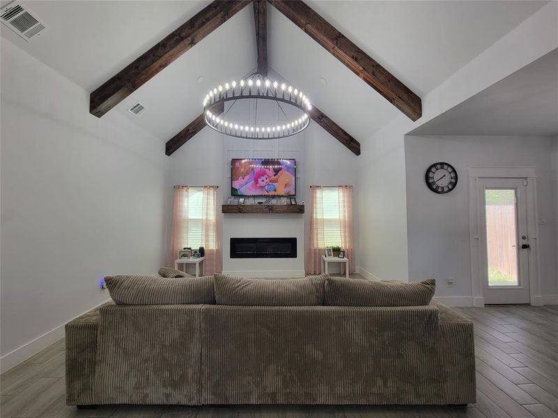 Living room with a glass covered fireplace, wood finished floors, and hanging lights