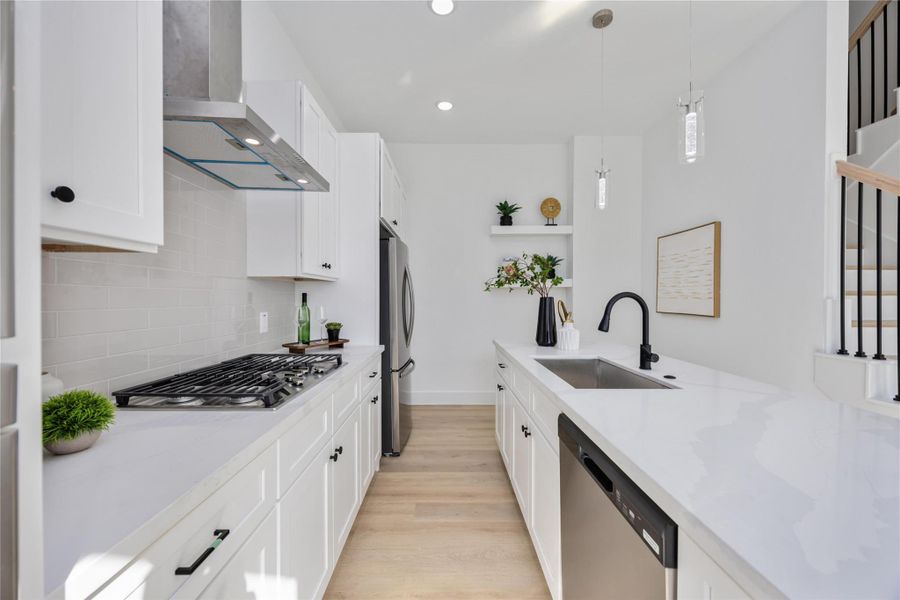 A bright, modern kitchen features sleek white cabinetry, stainless steel appliances, a stylish glossy subway-tile backsplash, and an extended quartz countertop accented with black fixtures and minimalist décor.