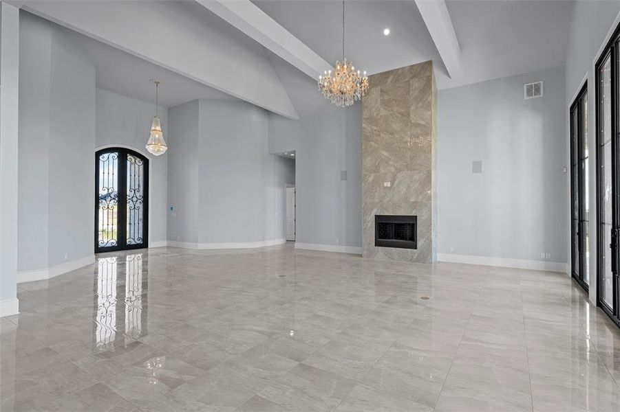 Unfurnished living room featuring beamed ceiling, a chandelier, french doors, arched walkways, and a towering ceiling Unfurnished living room featuring beamed ceiling, a chandelier, french doors, arched walkways, and a towering ceiling