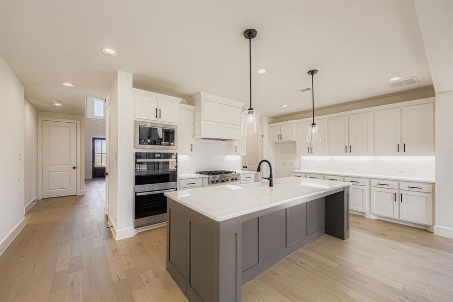 Kitchen with white cabinets, decorative light fixtures, light wood-style flooring, a kitchen island with sink, and appliances with stainless steel finishes