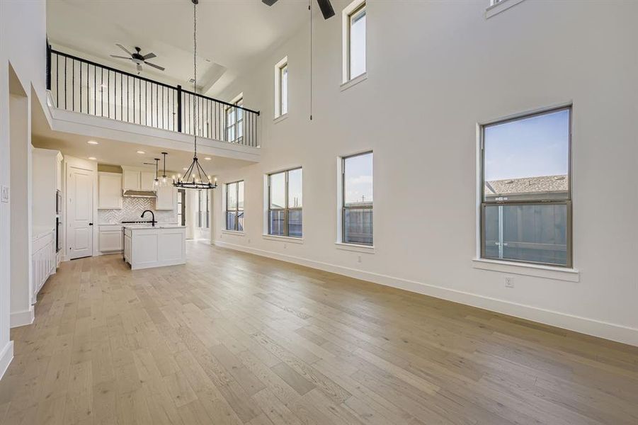 Unfurnished living room with light wood-style flooring, ceiling fan, a chandelier, and a towering ceiling