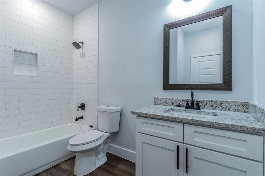 Full bathroom with hardwood / wood-style floors, tiled shower / bath, toilet, and vanity