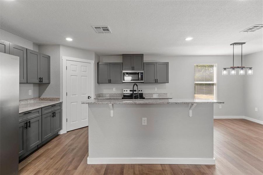 Kitchen featuring appliances with stainless steel finishes, light wood finished floors, gray cabinets, a kitchen bar, and a textured ceiling Kitchen featuring appliances with stainless steel finishes, light wood finished floors, gray cabinets, a kitchen bar, and a textured ceiling
