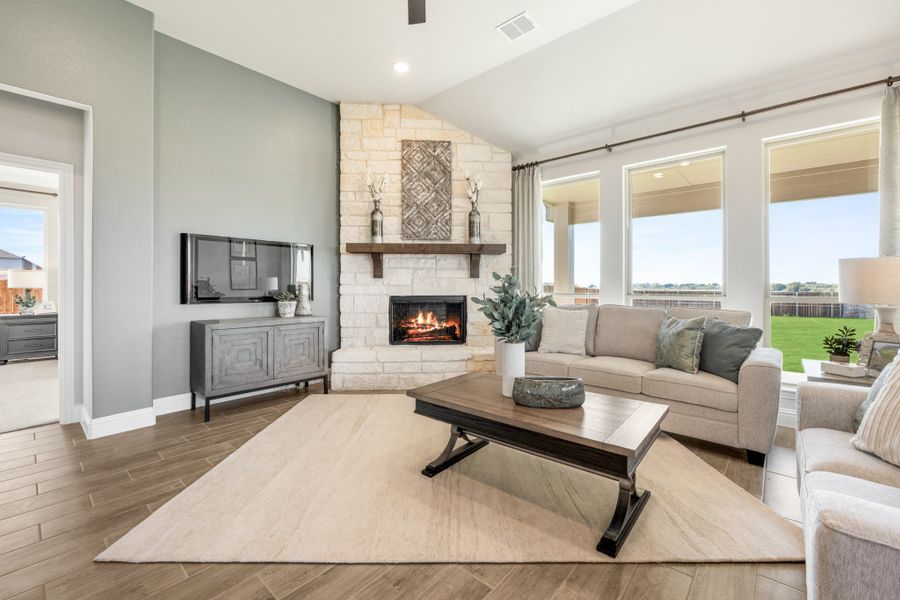 Living room with stone fireplace, vaulted ceiling, large windows, and wood-look tile floors