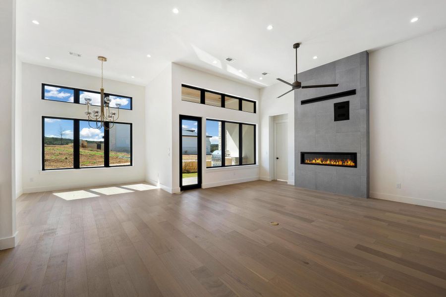 Unfurnished living room featuring a high ceiling, a fireplace, wood finished floors, suspended lighting, and ceiling fan