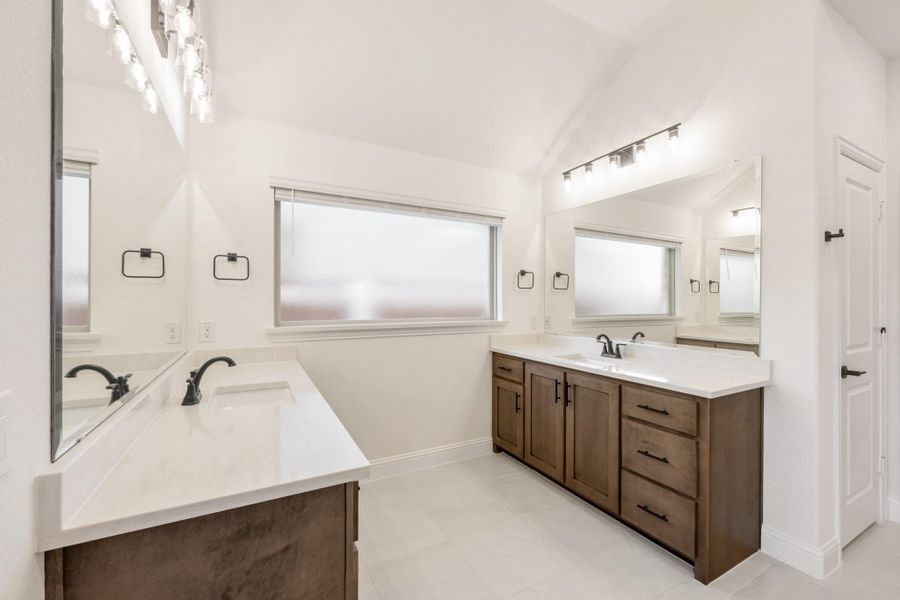 Bathroom with two separate vanities, dark wood cabinets, white countertops, and large mirrors with overhead lighting