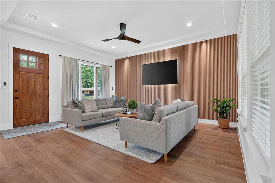 Living area featuring wood-finish flooring, a wood accent wall with integrated backlighting, recessed ceiling lights, and a modern ceiling fan