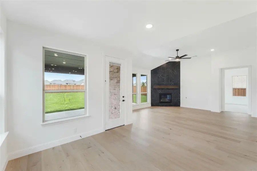 Open living room with light hardwood floors, dark tile fireplace, and ceiling fan