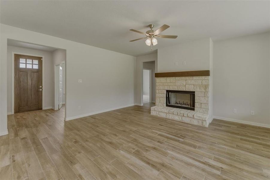 Spacious living area featuring wood-finish flooring, a stone fireplace with a wood mantel, a ceiling fan, and a paneled entry door with transom window
