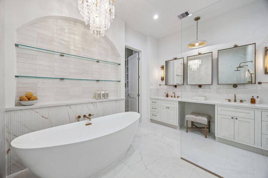 Another view of the 71" Soaking Tub with a Wall-Mounted Tub Filler in Champagne Bronze and a Light Glossy Bronze Finish Tiered Chandelier with Natural White Shell. There is also open glass shelving in the alcove wall that holds neatly stacked towels, jars, and bath accessories. Another view of the 71" Soaking Tub with a Wall-Mounted Tub Filler in Champagne Bronze and a Light Glossy Bronze Finish Tiered Chandelier with Natural White Shell. There is also open glass shelving in the alcove wall that holds neatly stacked towels, jars, and bath accessories.