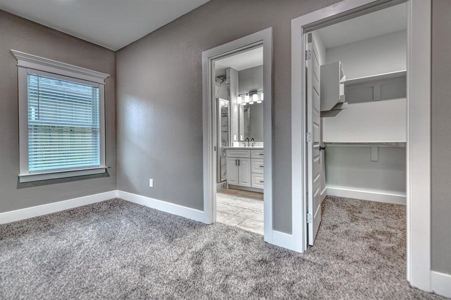 Unfurnished bedroom with a spacious closet, light carpet, and ensuite bathroom