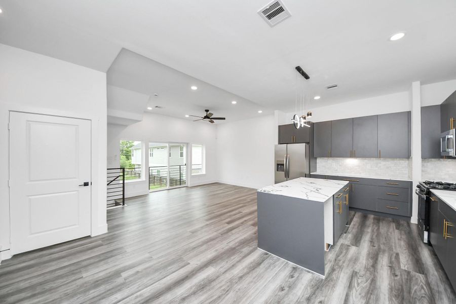 This modern open-concept kitchen and living area features sleek gray cabinetry, a marble-like patterned island, stainless steel appliances, and stylish light fixtures. The space is bright with ample natural light and elegant wood flooring, creating a spacious and inviting atmosphere. This modern open-concept kitchen and living area features sleek gray cabinetry, a marble-like patterned island, stainless steel appliances, and stylish light fixtures. The space is bright with ample natural light and elegant wood flooring, creating a spacious and inviting atmosphere.