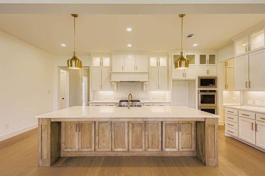 Kitchen with a large island with sink, glass insert cabinets, tasteful backsplash, recessed lighting, and light stone countertops