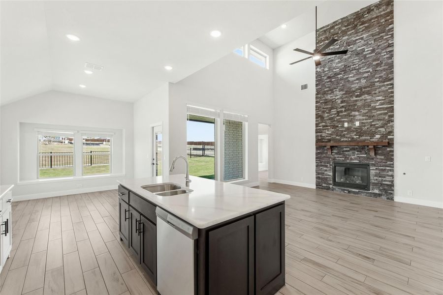 Open-concept kitchen and living area with large island, vaulted ceiling, and floor-to-ceiling stone fireplace