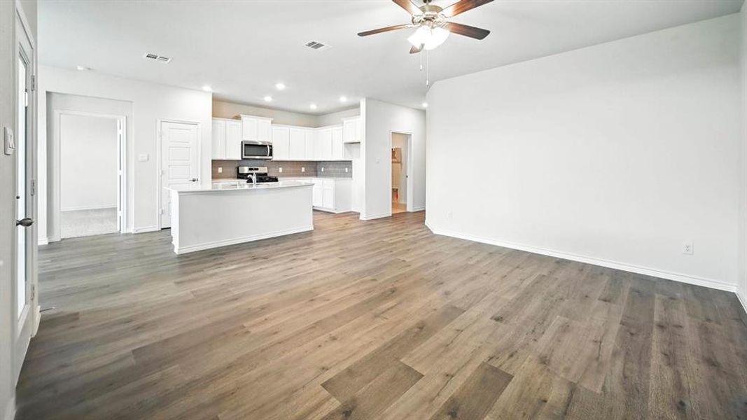 Expansive open-concept living space with wood-finish flooring, a ceiling fan with integrated lighting, and recessed overhead lighting